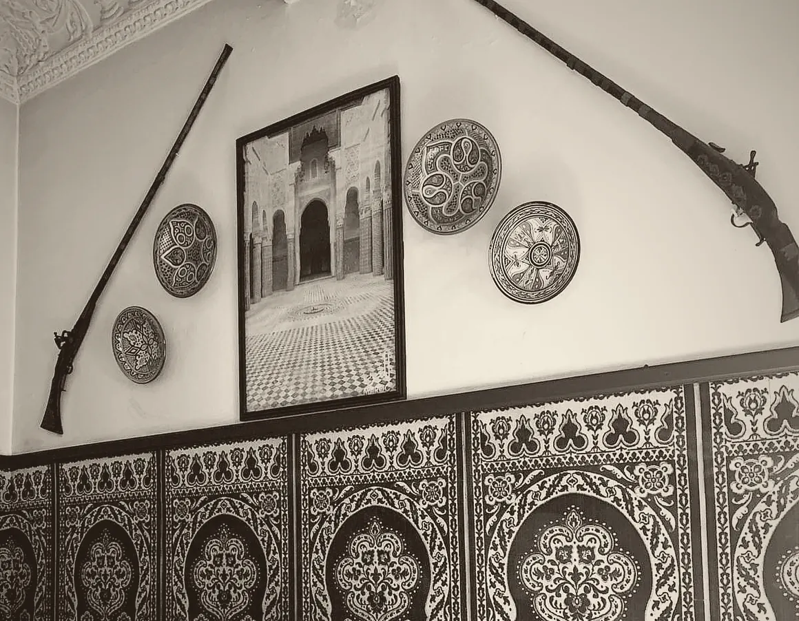 Salon de Restaurant Hamadi : plâtre sculpté, assiettes en céramique et fusils anciens accrochés au mur, boiserie damassée.