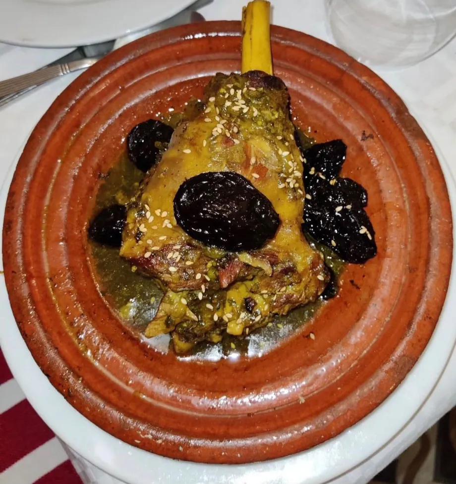 Tajine d'agneau aux pruneaux et sésame servi dans un plat en terre cuite.